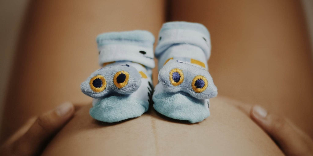 Cookie monster baby footies sitting on top of a pregnant mother's bare stomach