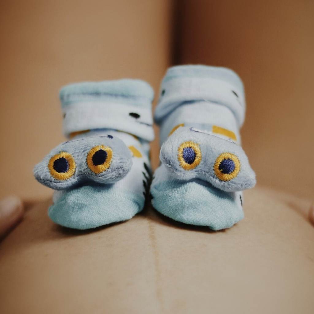 Cookie monster baby footies sitting on top of a pregnant mother's bare stomach